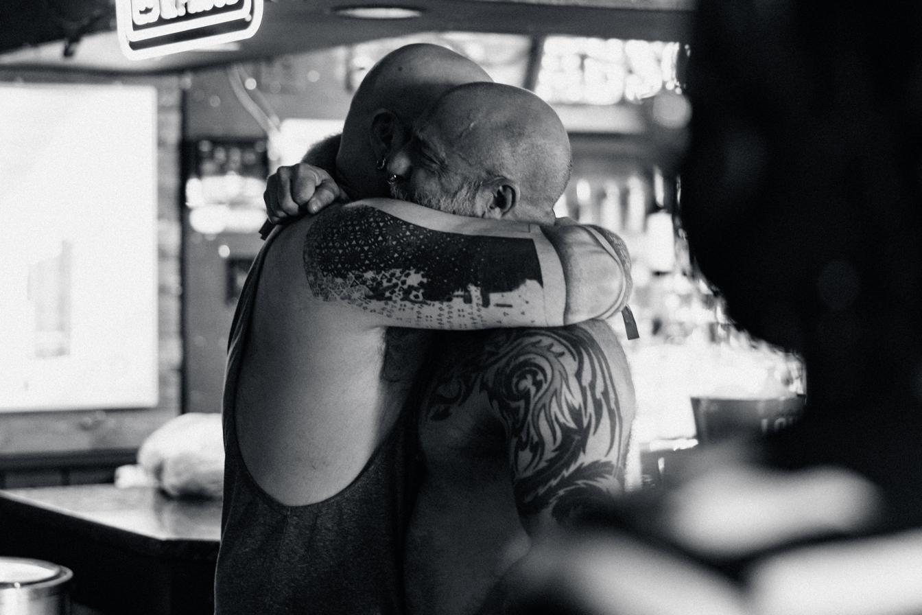 Black and white photo of Barclay Barrios embracing a friend, both with visible tattoos.